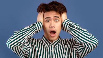 No Way, It's Unbelievable. Portrait of shocked scared asian guy emotionally reacting to news, grabbing his head with open mouth and looking at camera in amazement, isolated over purple background photo