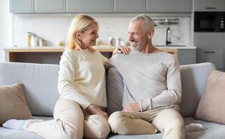 A joyful couple relaxes on a comfortable sofa in a modern living room, sharing smiles and affection while dressed casually in light-colored clothing. The warm atmosphere fosters their connection. photo