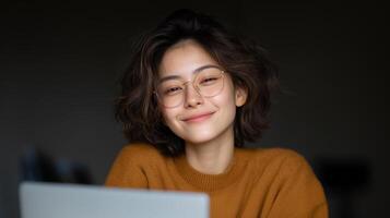 A woman with curly hair is smiling while interacting with a voice control assistant. She is wearing glasses and a cozy sweater, seated at a desk in a warm indoor setting during daylight. photo