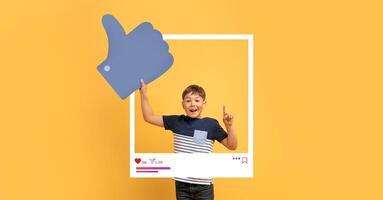 A cheerful child stands against a bright yellow background, holding a large thumbs up symbol while posing inside a social media frame. This fun setup captures the essence of online interactions. photo