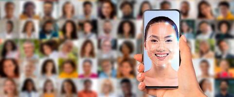 A hand holds a smartphone displaying a facial recognition scan of a person. Behind are various portraits of individuals, showcasing the technology's capabilities in identifying faces. photo