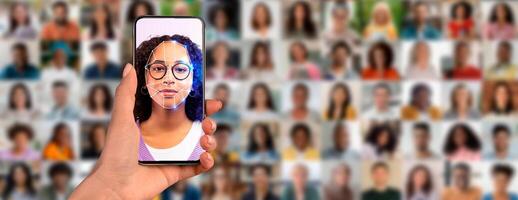 A person holds a smartphone displaying a facial recognition scan of their face, surrounded by a collage of diverse individuals in the background. photo