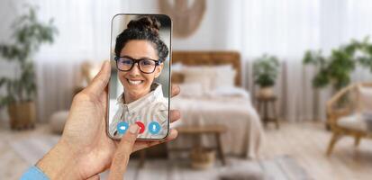A person holds a smartphone displaying a smiling individual on a call. photo