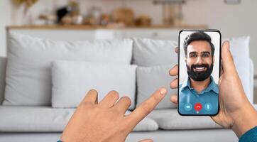 A person is using a smartphone to have an online call. The setting is a cozy home with a light-colored sofa in the background. The individual converses cheerfully. photo