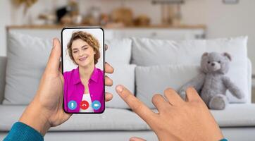 A person uses a smartphone to chat with someone while relaxing at home. The living room features a cozy couch and a teddy bear, creating an inviting atmosphere. photo