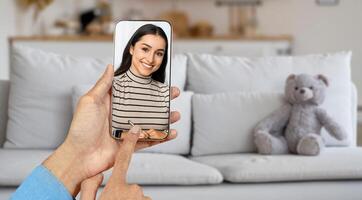A person interacts with a smiling individual on their smartphone screen while sitting in a cozy living room. The warm atmosphere contributes to an inviting virtual communication experience. photo