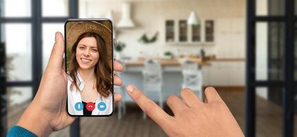A person using a smartphone for a chat in a home setting, showcasing a bright kitchen interior. The individual on screen smiles while communicating, reflecting a casual atmosphere. photo