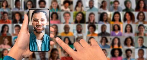 A person uses a smartphone to scan a face, utilizing modern recognition technology. The background features a collage of diverse faces, showcasing identification methods in a contemporary setting. photo