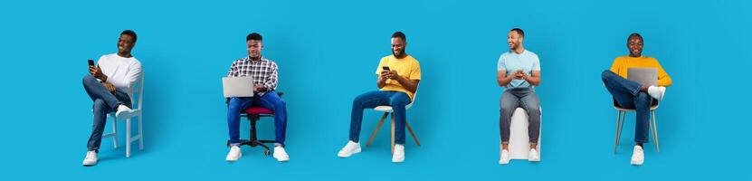 Four African American men interact with various digital devices in a bright blue background. They are seated on different chairs while showcasing a range of expressions and activities. photo