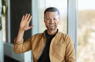 Man greets the camera while facial recognition technology analyzes his features. The setting reflects a contemporary office with natural light and greenery. photo