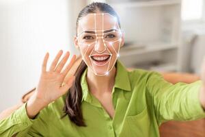 A woman smiles and waves while her face is scanned using modern facial recognition technology. This reflects how identification methods are evolving in everyday activities. photo