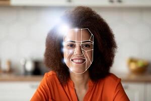 A woman smiles while modern facial recognition technology analyzes her face for identification. The setting is a well-lit kitchen, highlighting the integration of technology in daily life. photo