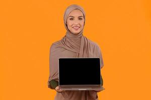 Muslim Woman Showing Blank Laptop Screen Recommending Internet Website Or Blog Standing Over Yellow Background. Arabic Female Computer User Showing Empty Display Advertisement. Mockup, Studio Shot photo