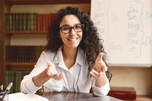 Online Tutoring. Friendly Woman In Glasses Having Conference, Teaching Foreign Languages, Talking And Gesturing At Camera During Web Call, Sitting At Desk In Home Office, Copy Space photo