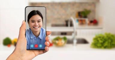 A person holding a smartphone for a call, showcasing a bustling kitchen in the background filled with fresh vegetables and a bright atmosphere. photo