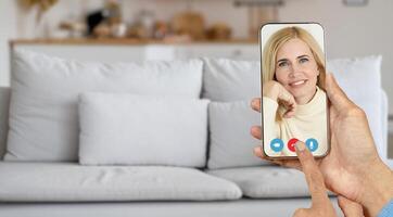 A person is having an online call at home, communicating through a smartphone with smiling senior woman. The relaxed setting is enhanced by a comfy couch in the background. photo