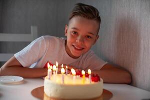 Smiling young boy leaning on a table with a lit birthday cake, enjoying a joyful celebration in a cozy setting. photo