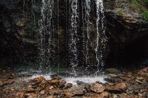 A cascading waterfall flows over a rugged rock formation, splashing onto wet stones below photo