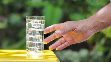 Hand Reaching for a Refreshing Glass of Ice Water on a Sunny Day with Greenery in the Background photo