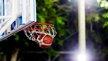 Dynamic Basketball Shot Mid-Air with Hoop and Net in Focus, Capturing the Excitement of Outdoor Sports at Night photo