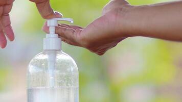 Close-Up of Hands Using Hand Sanitizer Dispenser Outdoors with Green Background photo