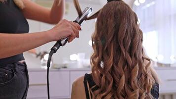 stylist creating curls for woman in chair using iron in cozy beauty salon concept of style and fashion video