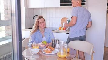 A couple enjoying a warm moment of breakfast with croissants, coffee and orange juice, sharing a laugh in their kitchen. Concept. lifestyle brands, family events, culinary experiences. video