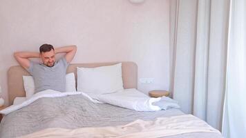 A man wakes up and stretches his muscles after sleeping on a bed in an apartment in the morning. Sleep and rest. video