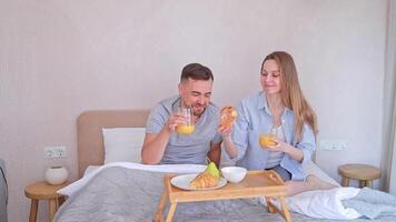 Married couple enjoying romantic breakfast in bed in the morning at home with croissants and orange juice video