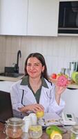 A nutritionist looking at the camera at a table with fruits and vegetables. Consultation on proper nutrition using a donut as an example of unhealthy food. video
