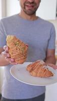 two sweet croissants on a plate in the hands of a man in the kitchen in the morning. Breakfast, pastries video