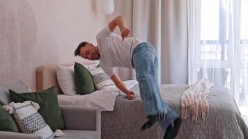 Man jumping cheerfully on a soft bed in an apartment. Travel and apartment rentals, rest and relaxation, vacation video