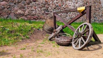 Old wooden cart wheels and wicker baskets near a stone wall in a rustic countryside setting photo