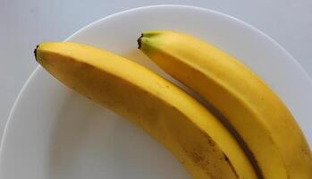 Two whole bananas on white plate closeup view stock photo