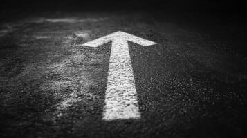 White arrow painted on dark asphalt road surface pointing forward symbolizing direction and progress in minimalistic style photo
