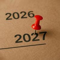 Red pin marks year 2027 on brown paper. Transition from 2026 to 2027 photo