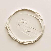 Circular smear of smooth, light beige cream on a matte surface, suggesting a dollop of cosmetic product or a gentle application photo