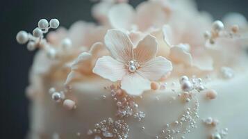 Macro close-up of a white cake decorated with a single pale pink sugar flower, small white pearls, and delicate sugar strands, highlighting the artistry and detail of the confection photo
