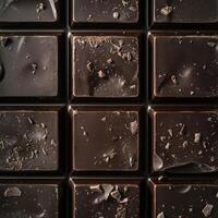 Top-down view of a dark chocolate bar, its smooth surface dusted with scattered chocolate chips. A tempting treat photo
