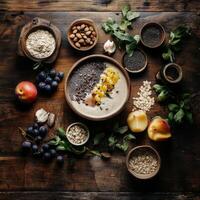 Overhead flat lay of a smoothie bowl surrounded by fresh ingredients like fruit, oats, nuts, and seeds on a wooden table photo
