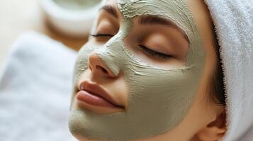 Close-up of a serene woman with closed eyes, wearing a grey clay facial mask and a white towel on her head, suggesting a calming spa skincare ritual photo