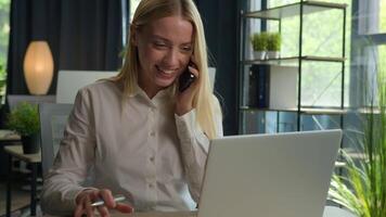 Happy Caucasian businesswoman talk phone conversation consult client business commerce in office smiling woman girl multitask working use laptop check documents on desk support customer mobile call video
