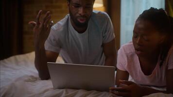 Irritated African American family using laptop bad connection at home night angry ethnic couple lying bed watch computer online movie series gesture negative reaction wifi bad failure bedroom evening video