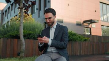 Caucasian businessman male leader worker employer typing message on mobile phone in city browsing social network use smartphone app smiling business entrepreneur outside office looking at camera smile video