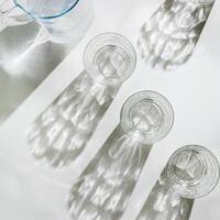 Water Glass with shadows at sunlight on white, delicate green blue color, minimal aesthetic top view shiny glasses at natural light, summer drink concept, pastel gradient interplay light and shadows photo
