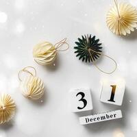 Flat lay of decorative ornaments and wood calendar date December 31st New Year's Eve, Minimal layout with paper festive decor beige balls and green Christmas Tree Ornament, honeycomb decor photo