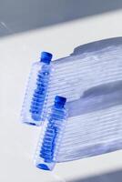 Transparent plastic bottles with blue caps and sun shadows on light background. Top view Water bottles at natural light. Themes of recycling, sustainability, water conservation, minimal photo