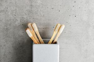 Bamboo toothbrushes with white bristles in square shaped grey concrete toothbrush holder. Natural wooden material, neutral colored photo. Sustainable living concepts, minimal style bathroom photo