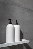 White bottles mock up on white shelf on gray concrete background, close up shampoo, conditioner. Aesthetic view beauty products in modern minimal bathroom neutral color. Side view, copyspace photo