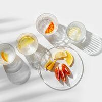 Citrus Infused Water in Glasses casting artistic light reflections and palm leaf shadows at sunlight. Summer drink concept, minimal pattern, flavored water with yellow red slices of fruit photo